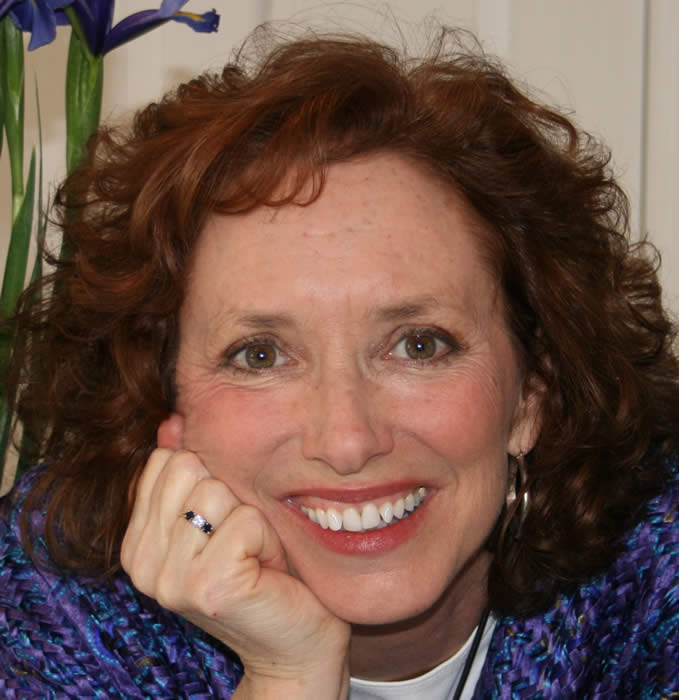 A woman with curly hair and white teeth smiling.