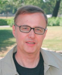 A man with glasses is standing in the grass.