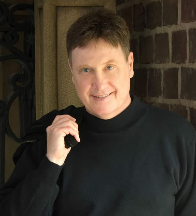 A man in black shirt holding his hand up to the side of his face.