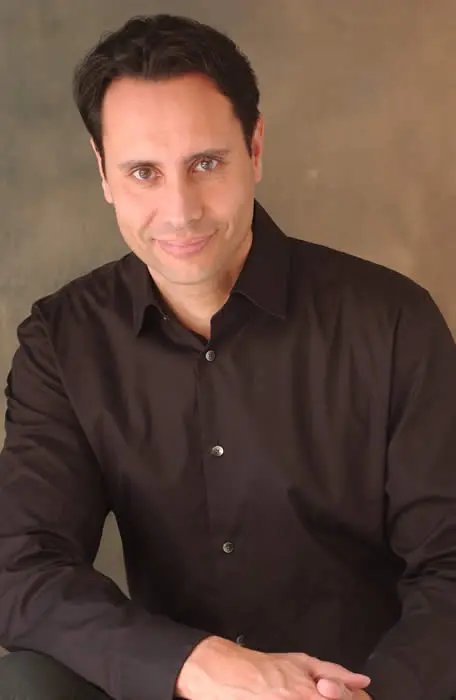 A man in black shirt sitting down with his hands crossed.