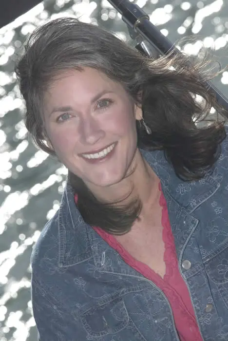 A woman smiling for the camera with her hair blowing in the wind.