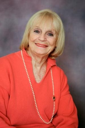 A woman in an orange shirt and pearls